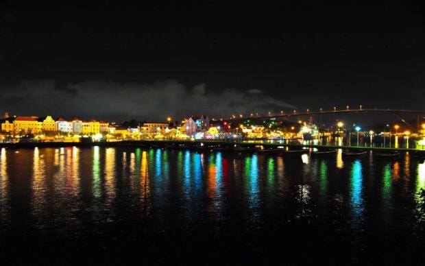 Colorful Curacao Island cityscape reflects on water at night with a bridge in the background