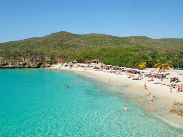 Clear turquoise water with tourists swimming near green hills on Curacao island shore