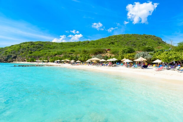 A beautiful Curacao beach with clear blue water and green hills under a bright sky
