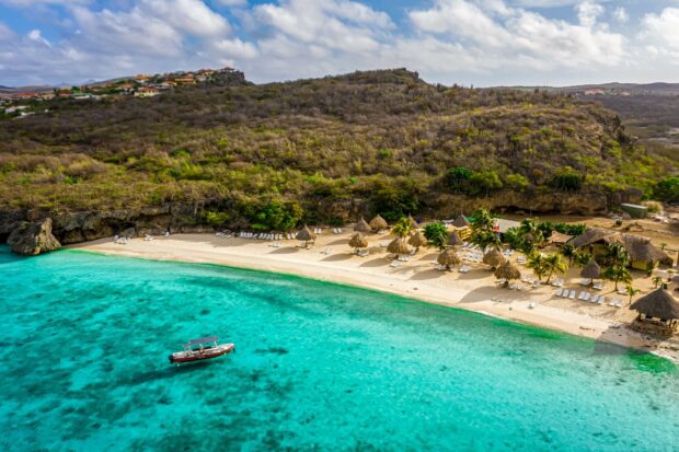 A scenic view of Curacao island with a beach and boat against clear turquoise water
