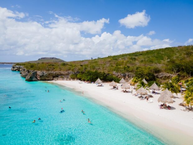 A scenic view of Curacao Island with clear turquoise water and a sandy beach surrounded by green hills