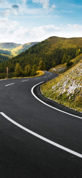 A winding road passes through lush green hills under a bright sky in Austria, 2K Phone Wallpaper