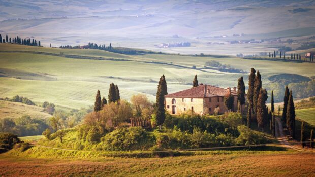A scenic view of cypress tree surrounded countryside with a rustic house on a hill