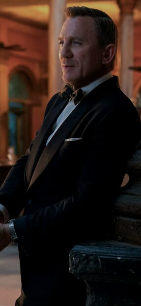 Daniel Craig dressed in a tuxedo stands near a stone railing in a dimly lit setting from No Time To Die, 2K Phone Wallpaper