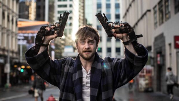Daniel Radcliffe holding two guns with a determined expression in a city street, HD Desktop Wallpaper