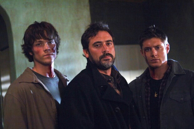 Sam Winchester and Dean Winchester with another man in a dark room showing serious expressions