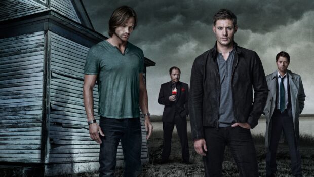 Dean Winchester stands near a weathered church in a dark cloudy setting with fellow hunters