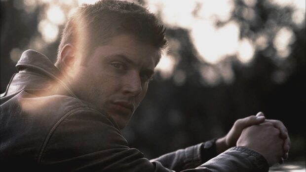 Dean Winchester sitting outdoors with folded hands during sunset