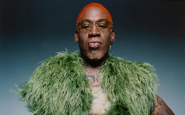 Dennis Rodman with orange hair and green feathered jacket displaying chest tattoos