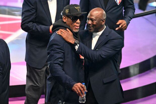 Dennis Rodman wearing a Chicago Bulls cap and sunglasses greeting a man in a suit at an event