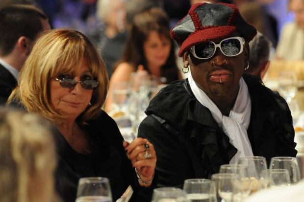 Dennis Rodman wearing a unique hat and sunglasses sitting at a formal event