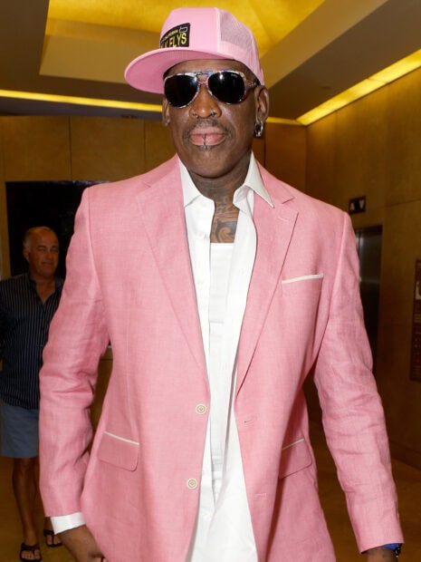 Dennis Rodman wearing a pink suit and hat with sunglasses indoors
