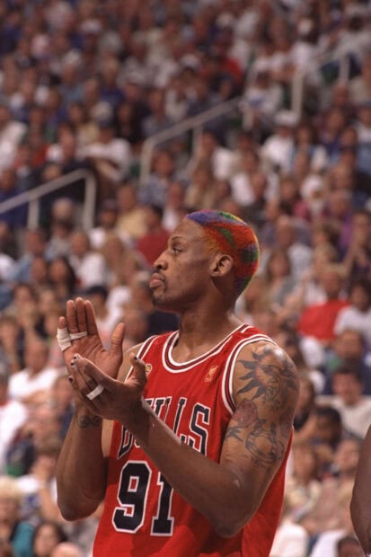 Dennis Rodman with colorful hair clapping during a basketball game wearing a bulls jersey number 91
