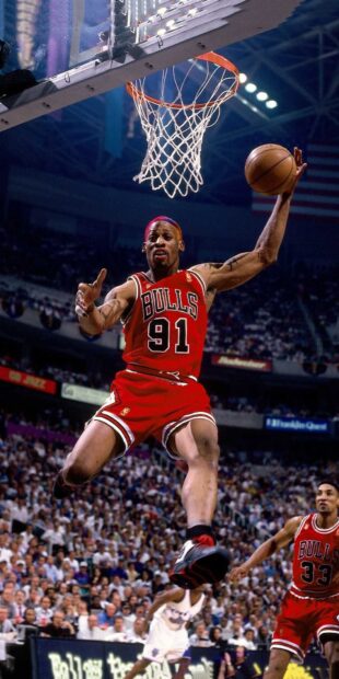 Dennis Rodman performing a basketball dunk during a game with crowd in the background