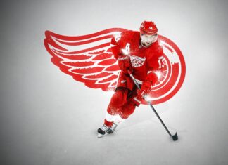 A Detroit Red Wings player skating with a hockey stick in front of the team logo