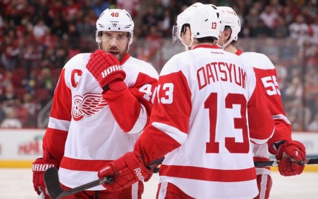 Detroit Red Wings players in white and red uniforms discussing on the ice during a game
