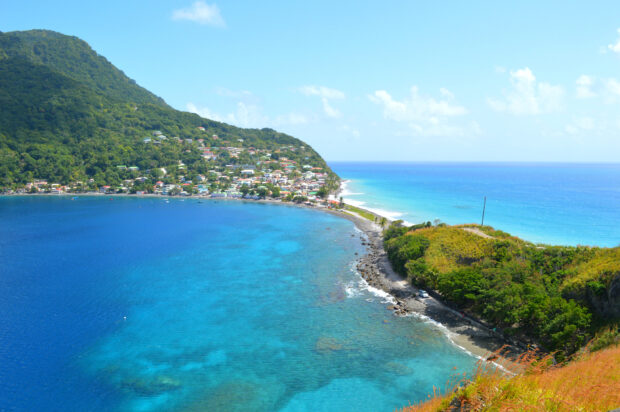 A panoramic view of Dominica Island with clear blue water and coastal houses under a bright sky, HD Desktop Wallpaper