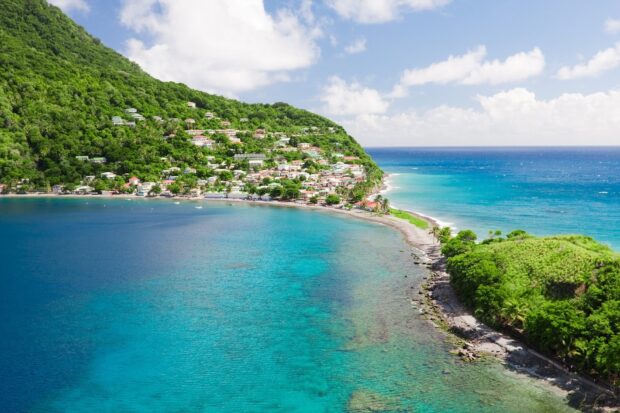 A scenic coastal village on Dominica Island surrounded by lush green hills and clear blue water, HD Desktop Wallpaper