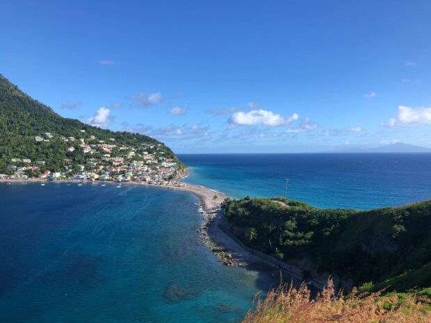A vibrant coastal view of Dominica Island with clear blue water and green hills, HD Desktop Wallpaper