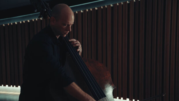 A man is focused on playing double bass with wooden panel background, HD Desktop Wallpaper