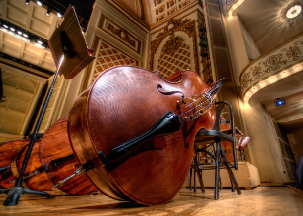 A double bass resting on the floor inside a decorated concert hall with chairs and music stands, HD Desktop Wallpaper