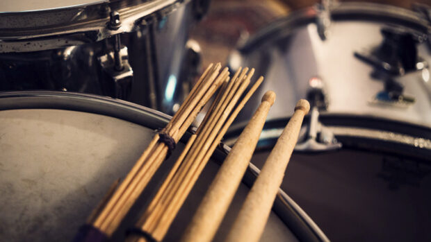 A close up view of drumsticks resting on the drum heads in a drum set with metallic surfaces, HD Desktop Wallpaper