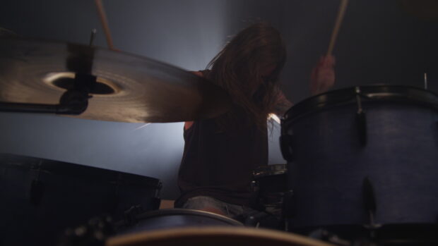 A drummer with long hair is passionately playing drums in a dimly lit room, 4K Desktop Wallpaper