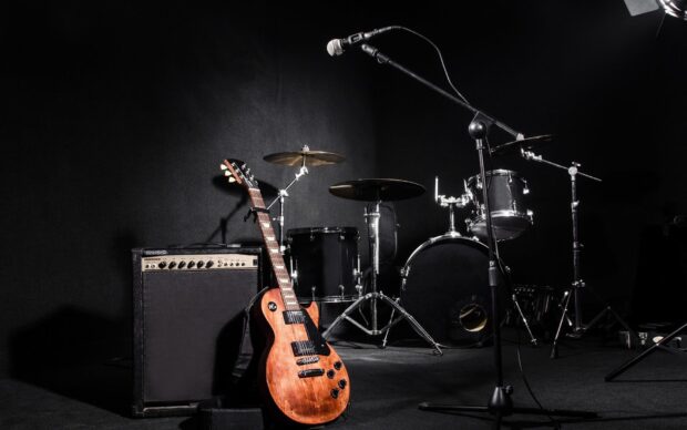 A drum set and electric guitar are placed together with a microphone stand in a dark music studio, HD Desktop Wallpaper