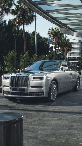 A silver Rolls Royce Phantom parked outside with trees and buildings in the background, 2K Mobile Wallpaper