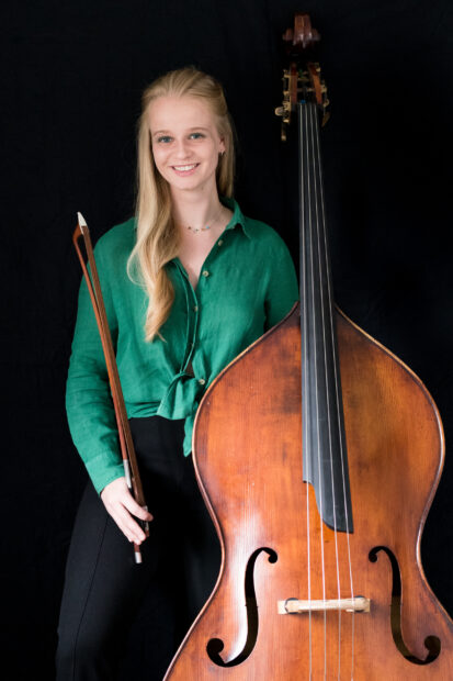A smiling woman poses with a double bass and bow in front of a black backdrop, 2K Portrait Wallpaper