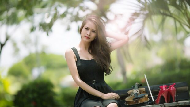 A young woman poses outdoors near a violin and shoes on a bench in a blurred garden, 4K Desktop Wallpaper