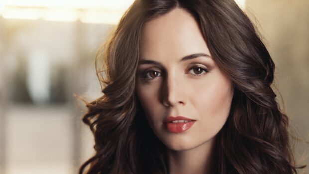 Eliza Dushku with flowing brown hair and natural makeup looking directly at the camera