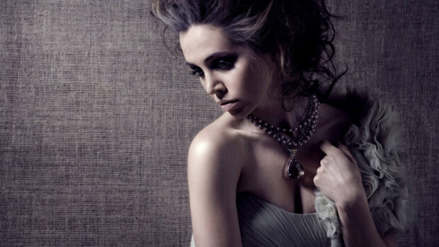 Eliza Dushku wearing a beaded necklace and elegant dress looking down thoughtfully