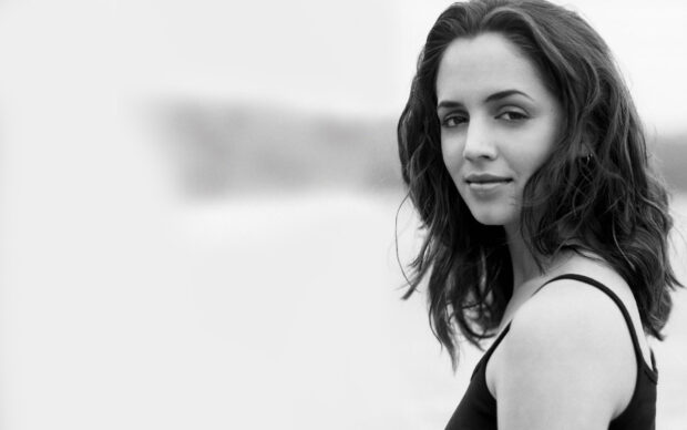 Eliza Dushku smiling softly in a black tank top outdoors in black and white