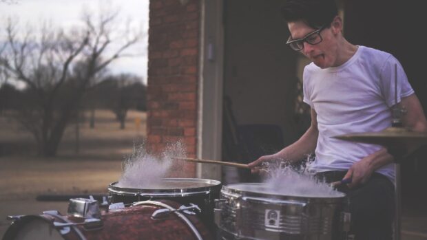 A young man intensely playing drums with drumsticks outside, HD Desktop Wallpaper