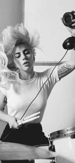 A female drummer holds drumsticks and headphones in a dynamic pose, 2K Phone Wallpaper