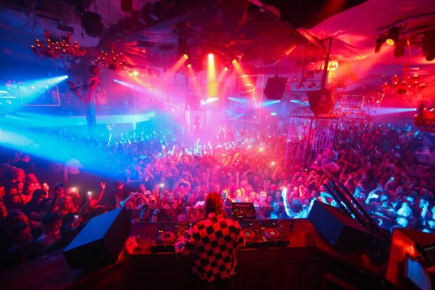 A DJ is performing in front of an energetic nightclub crowd with vibrant lighting effects, HD Desktop Wallpaper