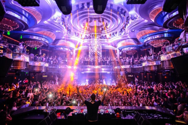 A DJ performs in front of a large crowd enjoying the vibrant nightclub atmosphere, HD Desktop Wallpaper