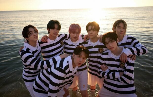 The Enhypen group is posing together in striped shirts near the water at sunset, HD Desktop Wallpaper