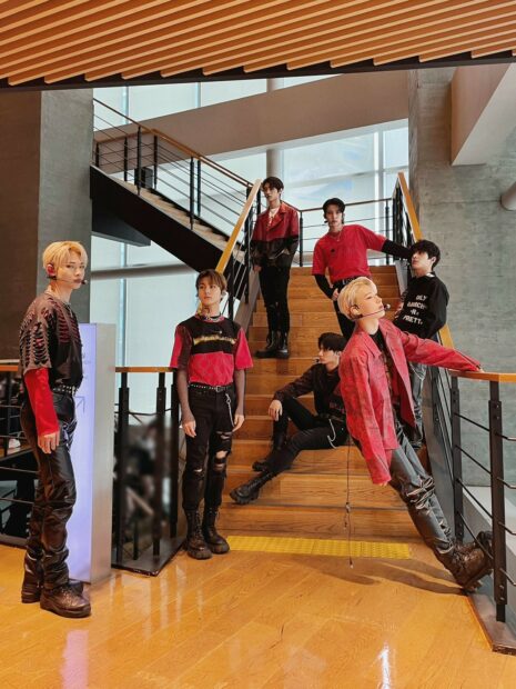The Enhypen members wear stylish red and black outfits in a modern stairwell, HD Mobile Wallpaper
