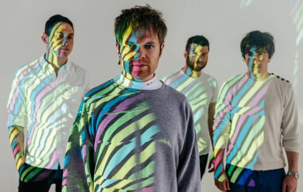 Enter Shikari band members stand with vibrant multicolored projections on their faces and clothes, HD Desktop Wallpaper