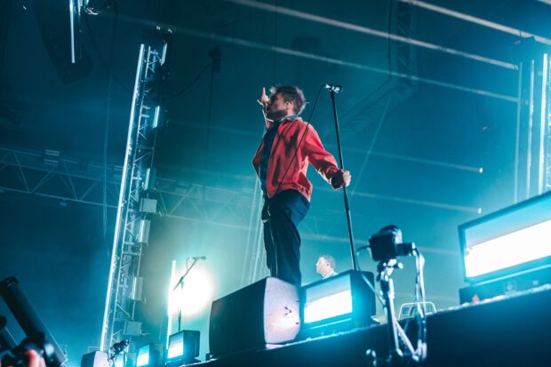 A lead singer of Enter Shikari band raises his hand while performing on stage with bright lights, HD Desktop Wallpaper