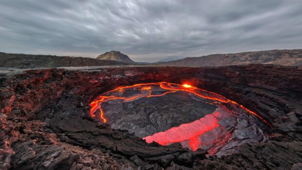 The Ethiopia volcanic lava flow is captured under a cloudy sky with surrounding rocky terrain, 2K Desktop Wallpaper