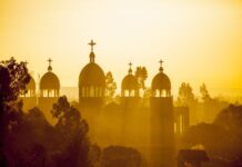 The sun shines through the domes and crosses of an Ethiopian church surrounded by trees, 2K Desktop Wallpaper