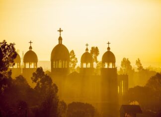 The sun shines through the domes and crosses of an Ethiopian church surrounded by trees, 2K Desktop Wallpaper