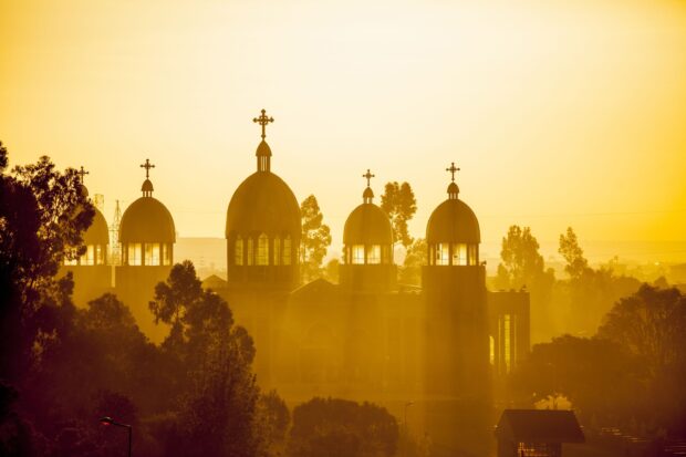 The sun shines through the domes and crosses of an Ethiopian church surrounded by trees, 2K Desktop Wallpaper