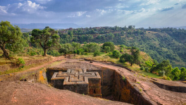 An ancient stone church carved into rock surrounded by green hills in Ethiopia, 2K Desktop Wallpaper