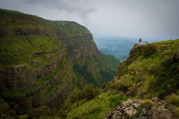 A person standing on a rocky cliff overlooking the vast green mountains of Ethiopia, 2K Desktop Wallpaper