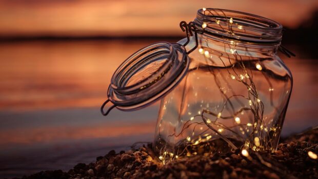 Glass jar filled with fairy lights resting on rocky surface during sunset
