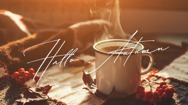A steaming mug on a cozy blanket with a cursive hello greeting for the start of Fall season